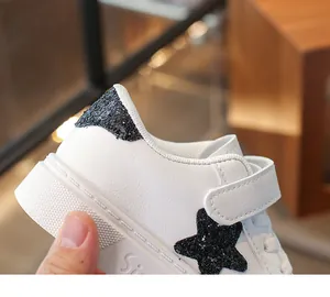 Detailopname van witte kindersneaker met een zwarte glitterster en klittenbandsluiting.