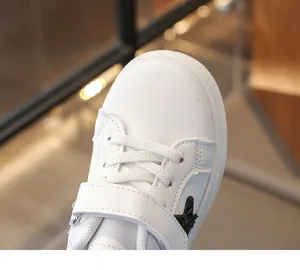 Detailopname van witte leren kindersneakers met een zwart sterpatroon erop.