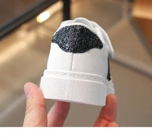 Close-up van de hiel van witte leren kindersneakers met een zwarte glitterster-patch