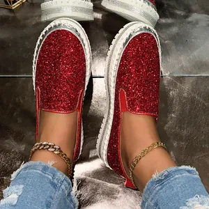 Close-up view of sparkling red glitter slip-on loafers worn with stylish golden anklets