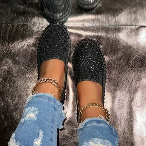 Close-up of black glitter slip-on loafers with gold chain anklet and distressed jeans.
