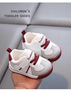Close-up of white and burgundy soft-soled toddler shoes held in hand with Velcro
