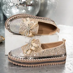 Primer plano de mocasines de lentejuelas doradas con punta de strass y lazo decorativo