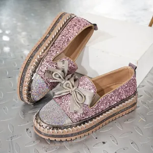 Detalle de mocasines con plataforma rosa brillante con lazo de pedrería y puntera.