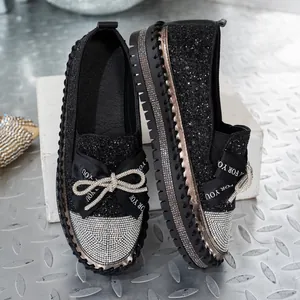 Detalle de mocasines negros de purpurina con lazo de pedrería y puntera brillante