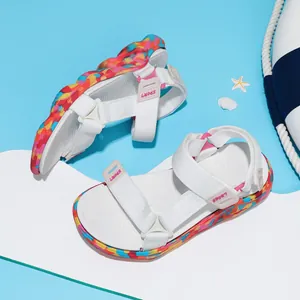 Sandales d'été pour filles avec lanières blanches et semelles colorées sur fond bleu de plage