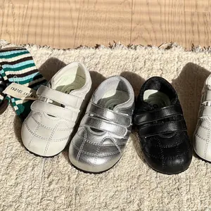 Scarpe primi passi morbide per neonati in bianco, argento e nero con chiusura a strappo.