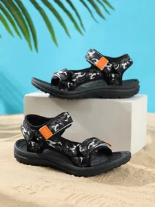 Detailed view of children's camouflage sandals with orange straps on beach sand background