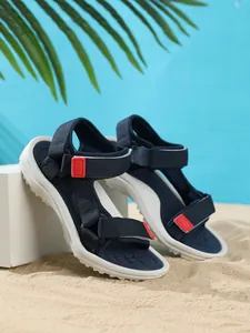 Detailed side view of navy blue kids beach sandals with red accents on natural sand