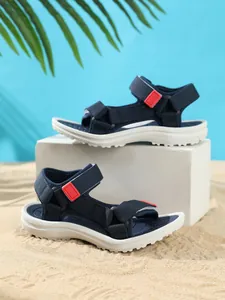 Detailed side view of navy blue kids' beach sandals on sand with summer vibes backdrop.