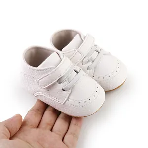 Close-up of white baby shoes showing faux leather texture and velcro strap on a hand