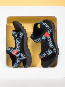 Close-up of children's camo pattern sandals with red buckles on yellow background.