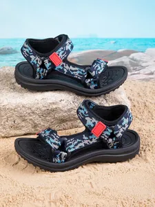 Detailed side view of blue camouflage kids beach sandals placed on a sunny seaside rock.