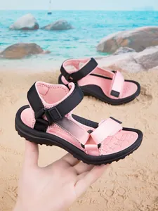 Detail view of pink and black children's sandals being held over a sunny beach background.