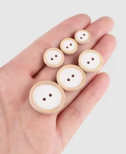 Hand holding various sizes of natural poplar wood buttons for high-end clothing detailing