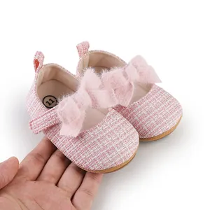 Detailaufnahme der rosa Tweed-Babyschuhe mit großer Plüschschleife in der Hand