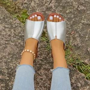 Nahaufnahme von silbernen Metallic-Sandalen für Damen, getragen auf einem Natursteinweg