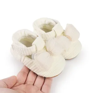 Close-up of cream baby walking shoes with a large mesh bow held in a hand for scale