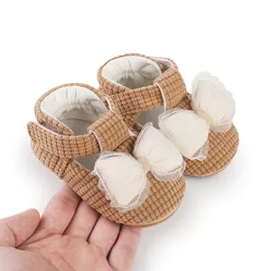 Detailed view of brown corduroy baby walking shoes with large white lace bows held in hand