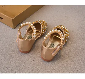 Close-up detail of girl's sparkling gold sandals with pearl straps and sequins.