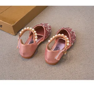 Close-up of pink sequined girls' princess shoes with pearl straps on gray background.