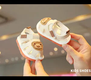Detailed close-up of beige baby sandals with cartoon bear patch and orange soft soles.