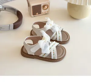 Primer plano de sandalias blancas para niña con lazos de tul y bordados de flores