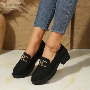 Detalle de mocasines negros para mujer con tacón grueso y elegantes hebillas doradas.