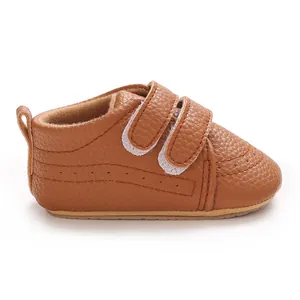 Gros plan sur une chaussure pour bébé en simili cuir marron avec double bride auto-agrippante.