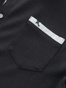 Nahaufnahme von schwarzem Waffelstrick mit einer Brusttasche mit weißem Rand und blauer Stickerei