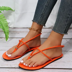 Dettaglio di eleganti sandali bassi infradito arancioni con accenti metallici su modella