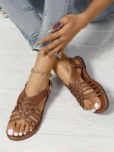 Detalle de sandalias planas de cuero trenzado marrón con correas cruzadas y hebilla