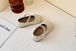 Detail view of cream children's Mary Jane shoes with elegant braided strap detail.