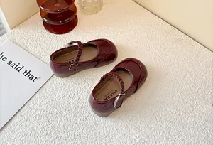 Detail of burgundy children's Mary Jane shoes with braided strap and glossy finish.