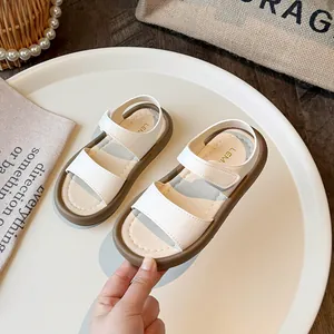 Minimalist white girls' sandals with soft brown soles and Velcro straps on a white tray