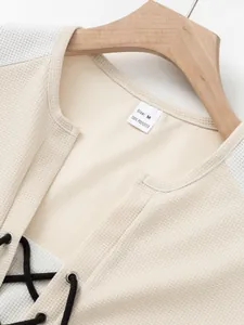 Detailed view of beige waffle knit t-shirt featuring black lace-up front and silver eyelets