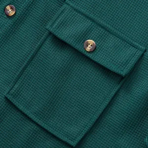 Macro shot of dark green waffle knit fabric showing chest pocket and amber buttons.