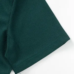 Macro detail of dark green waffle knit fabric and stitched hem on mens casual t-shirt