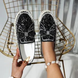 Detailed view of black sequined slip-on sneakers with a large rhinestone bow and thick sole.