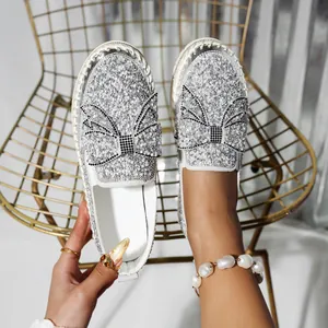 Macro shot of stylish silver glitter slip-on loafers featuring a luxury rhinestone bow design