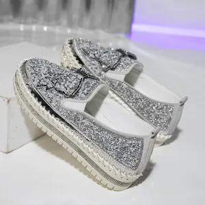 Detail of silver glitter slip-on loafers with a sparkling rhinestone bow and thick sole.