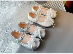 Detail of girls' Mary Jane shoes with lace bows and pearl straps in cream and silver.