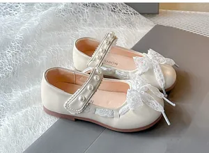 Close-up of elegant ivory girl shoes featuring lace bow and pearl strap details.