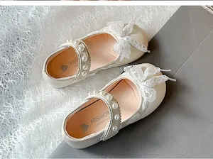Exquisite detail of girls' white Mary Jane shoes with lace bow and pearl strap decoration.