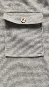 Close-up detail of grey waffle knit fabric featuring a front pocket and brown button