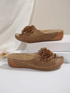 Gros plan de mules à semelles compensées marron avec fleur décorative et perforations