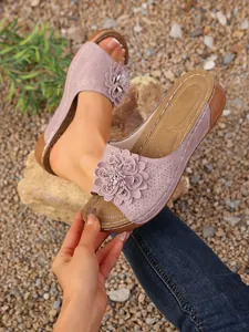 Gros plan sur des mules à talons compensés roses avec décoration florale et bout ouvert