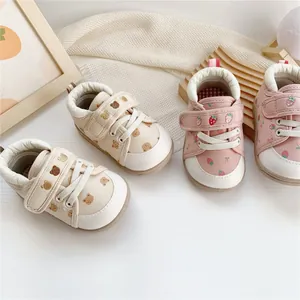 Detailed view of baby walking shoes with bear and strawberry patterns and velcro straps