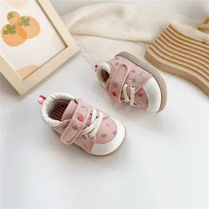 Close-up of pink baby walking shoes with cute strawberry patterns and velcro straps.