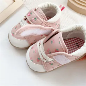 Close-up detail of pink baby walking shoes with strawberry patterns and velcro strap